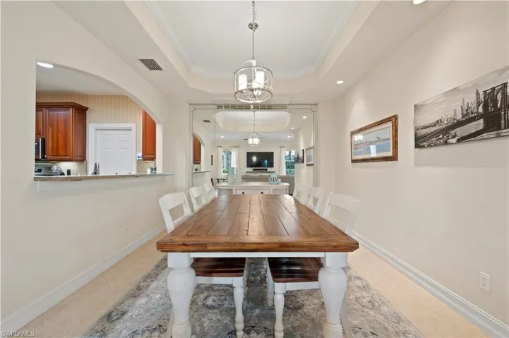 Dining room featuring a raised ceiling, crown molding, light tile patterned flooring, recessed lighting, and arched walkways
