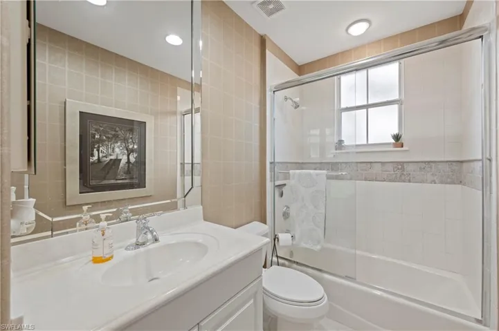 Bathroom featuring vanity, shower / bath combination with glass door, and tile walls