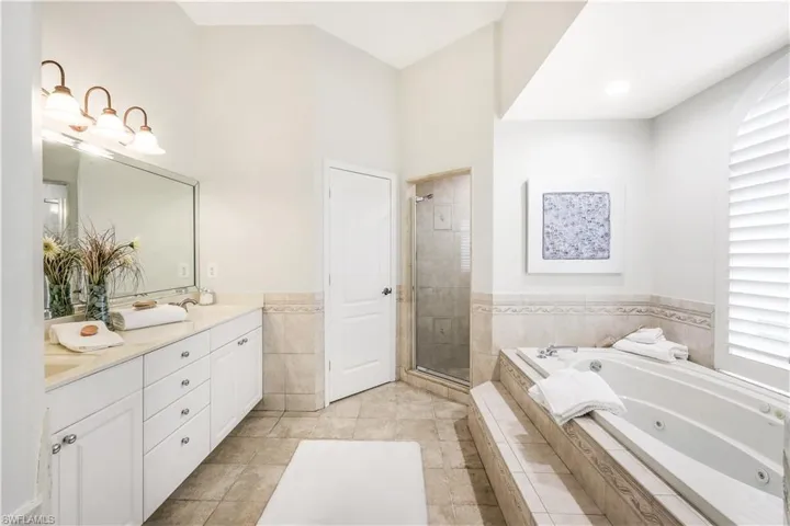 Primary bathroom with tile patterned flooring, double vanity, walk-in shower and jacuzzi tub.