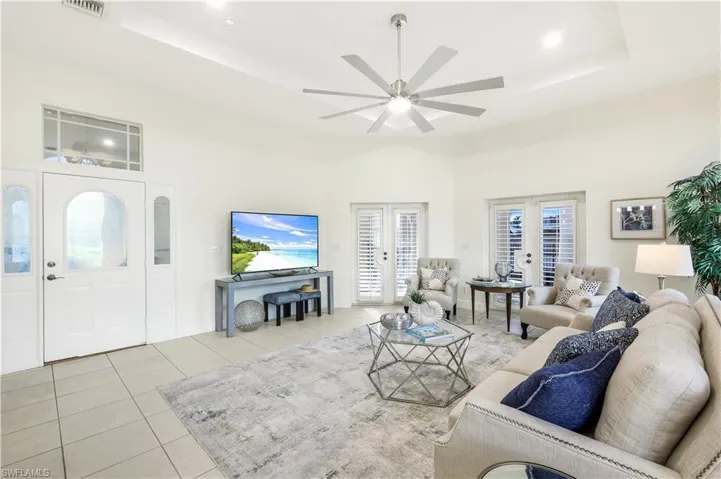 Tiled living room featuring ceiling fan, a raised ceiling, and french doors to front lanai.