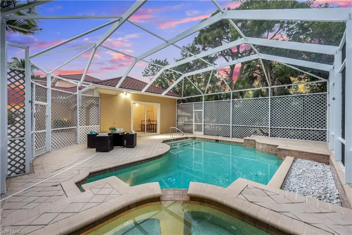 Pool at dusk featuring an in ground hot tub, a patio, and a lanai