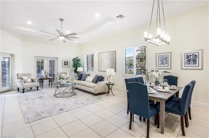 Tiled dining area featuring ceiling fan with notable chandelier and a raised ceiling.