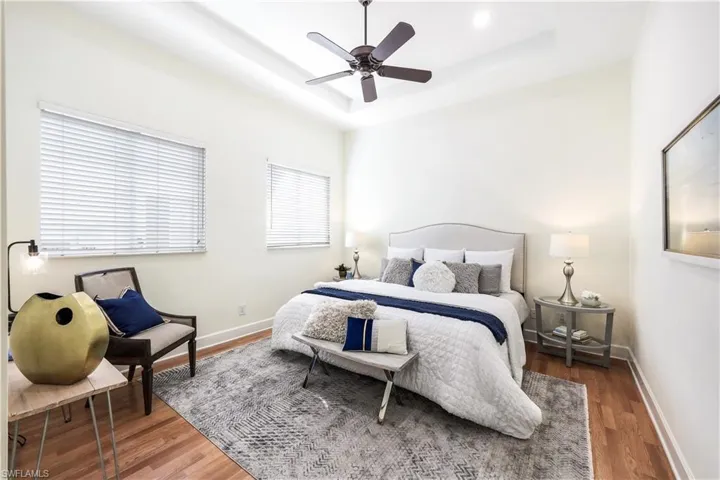 Primary bedroom with hardwood flooring, large windows, ceiling fan, and a tray ceiling.