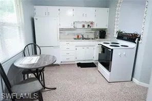 Kitchen with sink, white cabinets, light colored carpet, and white appliances