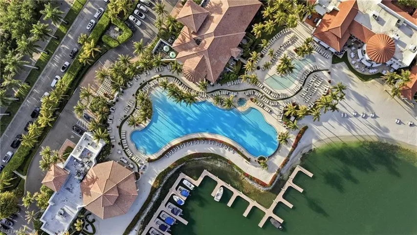 Waterfront community complex featuring a large swimming pool, paved pool deck, boat slips, and terracotta-tiled roof structures