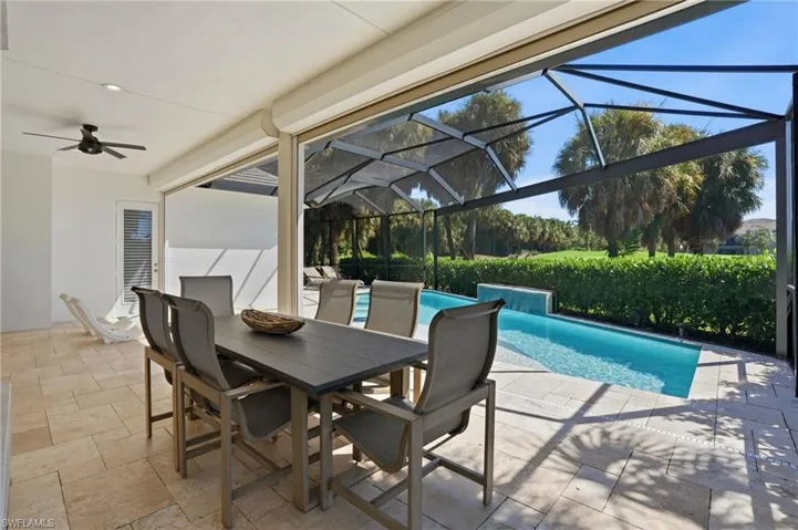 Covered patio featuring stone-tile flooring and a ceiling fan, opening to a screened-in pool area with a water feature
