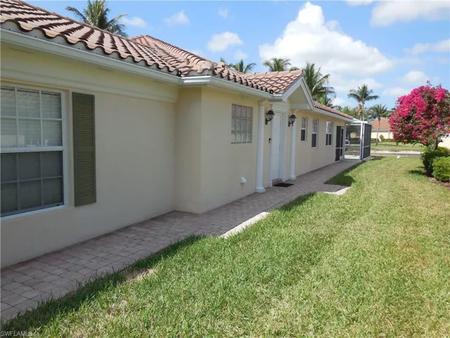 View of side of home featuring a lawn, stucco siding, a tile roof, and a lanai