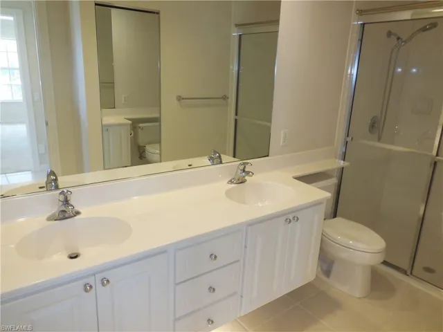 Full bathroom featuring a shower stall, double vanity, and light tile patterned floors