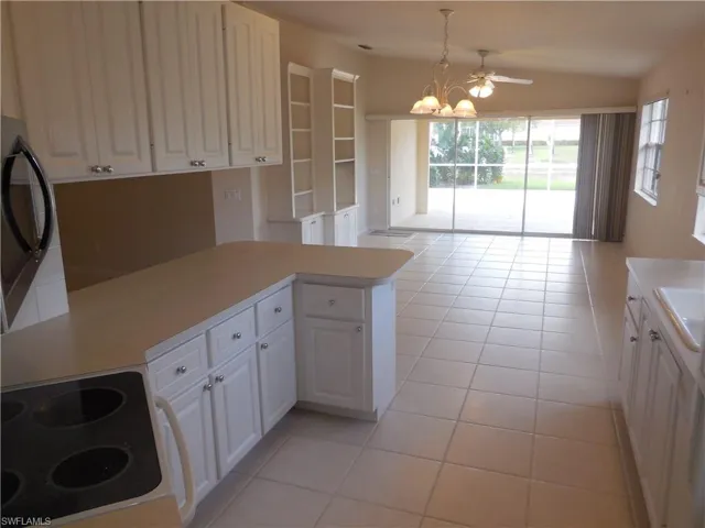 Kitchen featuring electric stove, light tile patterned floors, light countertops, stainless steel microwave, and vaulted ceiling