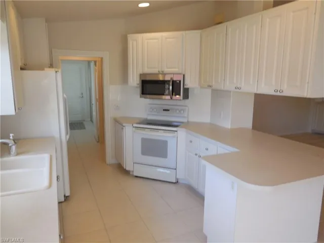 Kitchen featuring a peninsula, white appliances, white cabinets, light countertops, and light tile patterned floors