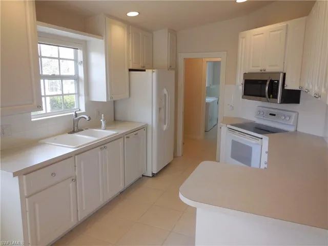 Kitchen with decorative backsplash, white appliances, white cabinetry, light countertops, and recessed lighting