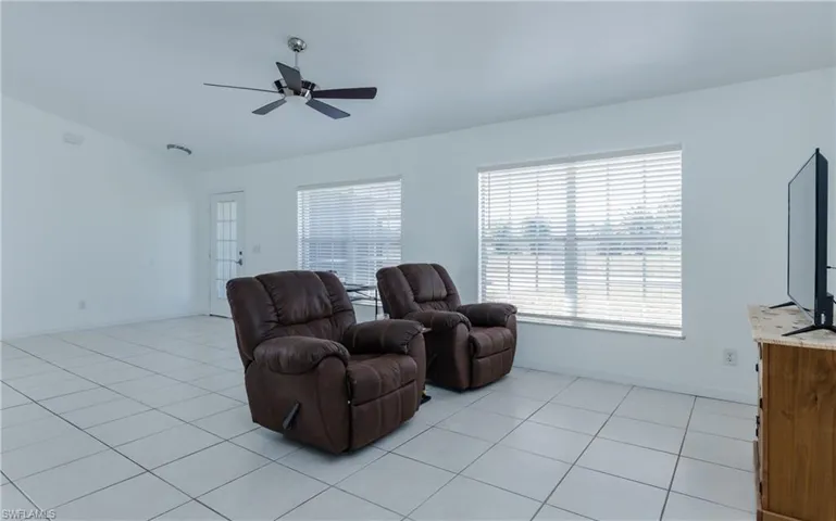 Living area with vaulted ceiling, light tile patterned flooring, a ceiling fan, and baseboards