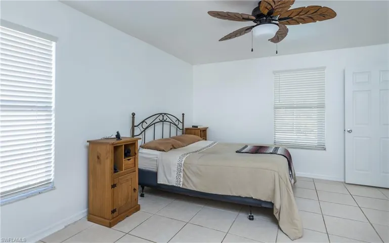 Bedroom featuring multiple windows, light tile patterned floors, a ceiling fan, and baseboards