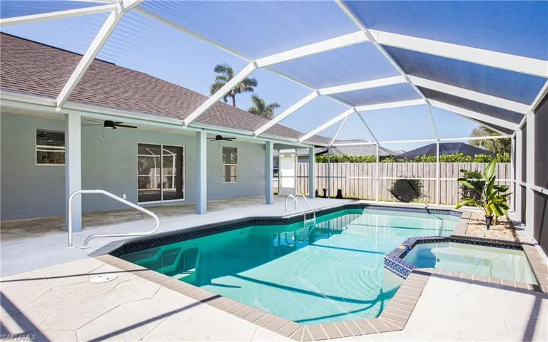 View of pool with glass enclosure, fence, a pool with connected hot tub, ceiling fan, and a patio area