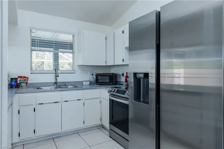 Kitchen featuring a sink, stainless steel appliances, light tile patterned flooring, and white cabinetry