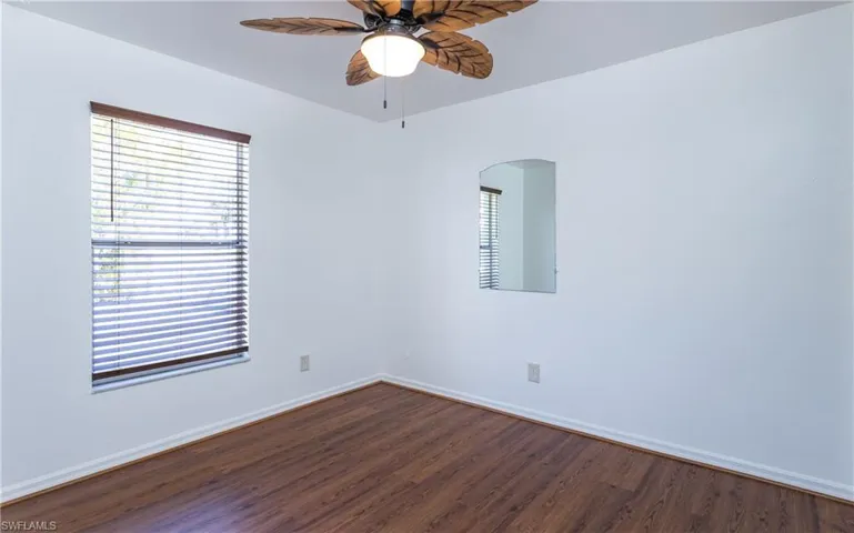 Empty room featuring baseboards, arched walkways, dark wood finished floors, and a ceiling fan