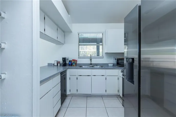 Kitchen with light countertops, light tile patterned flooring, white cabinets, black appliances, and a sink