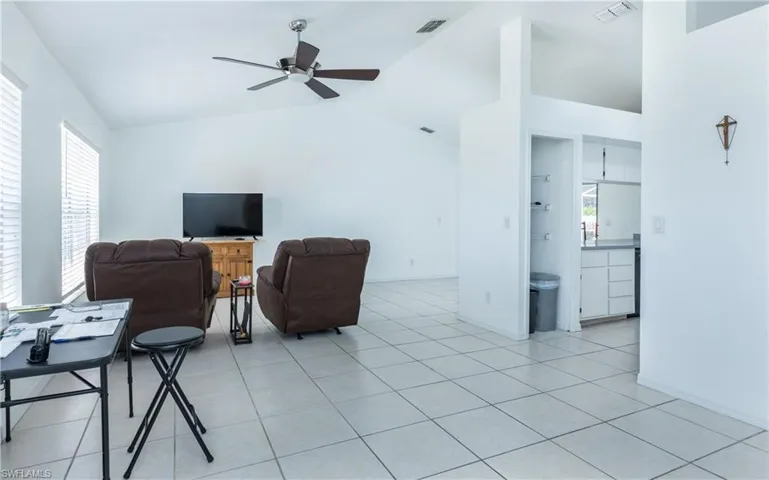 Living area with light tile patterned floors, visible vents, and vaulted ceiling