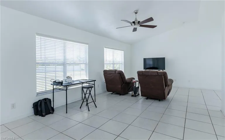 Living area with vaulted ceiling, light tile patterned flooring, baseboards, and ceiling fan