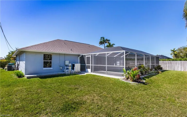 Rear view of house featuring glass enclosure, a lawn, central AC, and fence