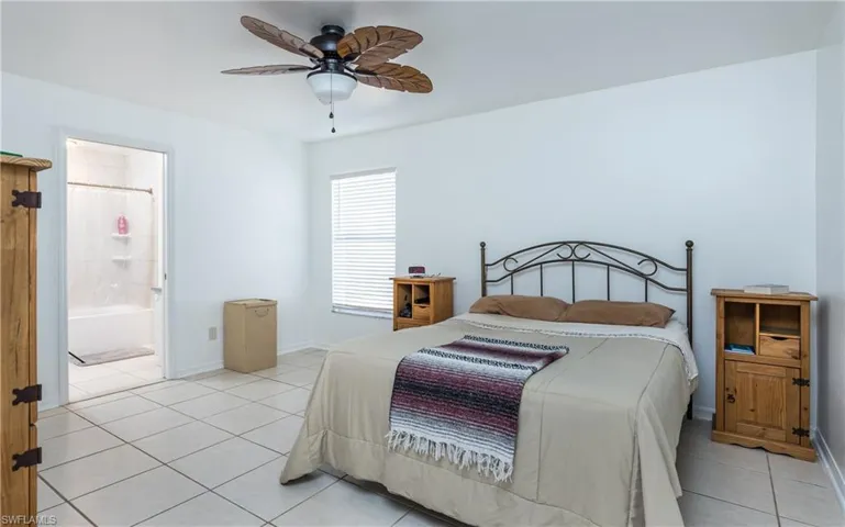 Bedroom featuring light tile patterned floors, baseboards, ensuite bath, and a ceiling fan
