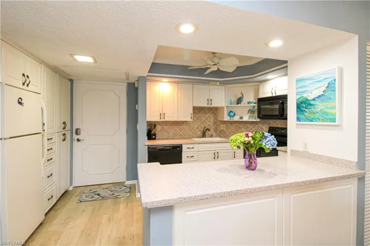 Kitchen featuring decorative backsplash, a peninsula, light wood-type flooring, black appliances, and a sink