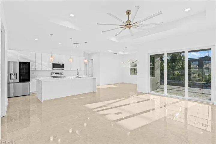Unfurnished living room featuring a tray ceiling, recessed lighting, a chandelier, ceiling fan, and light marble finish floors