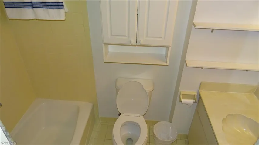 Bathroom featuring a white bathtub with yellow tiled surround, toilet, and a vanity with an integrated sink