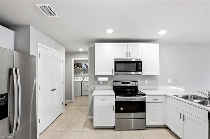 Kitchen featuring stainless steel appliances, light countertops, washer and clothes dryer, white cabinets, and light tile patterned floors