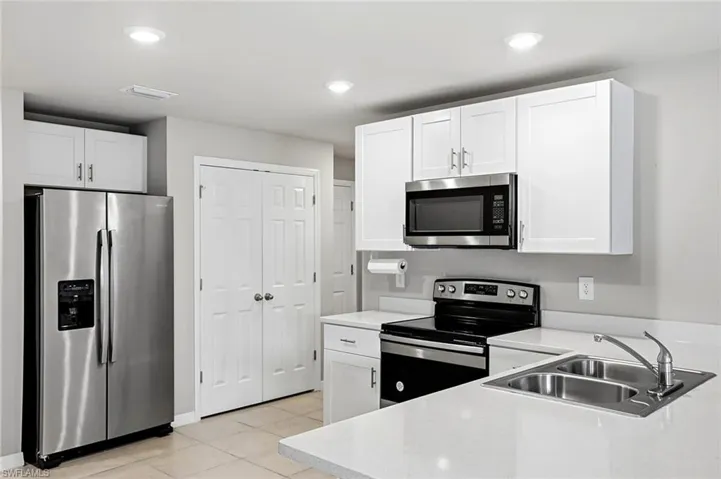 Kitchen with stainless steel appliances, white cabinetry, light tile patterned floors, and recessed lighting
