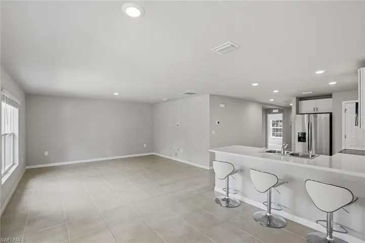 Kitchen with a kitchen bar, a peninsula, stainless steel fridge, white cabinetry, and recessed lighting