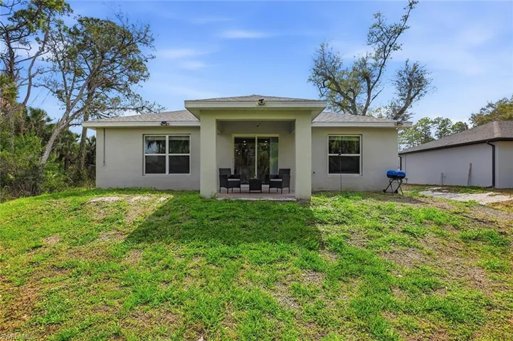 Back of house featuring a patio, stucco siding, a yard, and a shingled roof