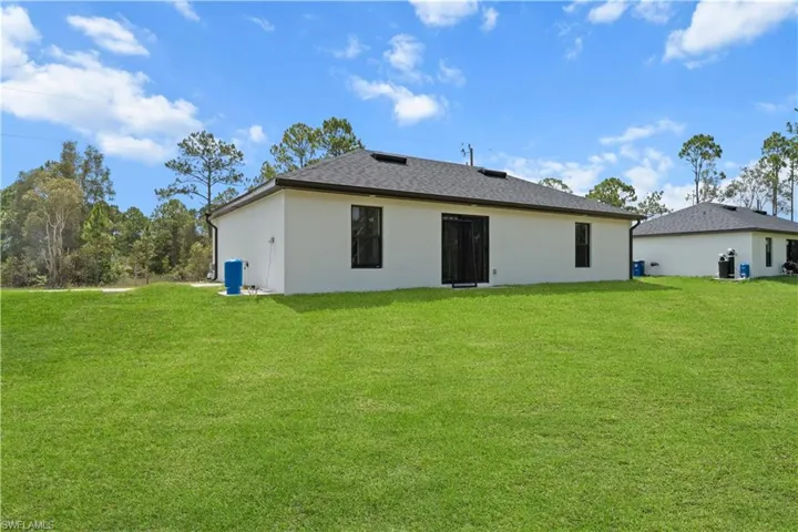 Rear view of house featuring a yard, stucco siding, and a shingled roof