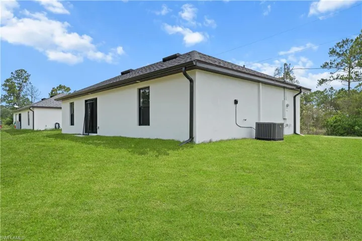 Back of property with stucco siding, a lawn, and a shingled roof