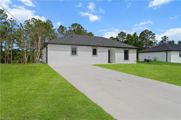 View of front facade featuring driveway, a front lawn, stucco siding, and roof with shingles