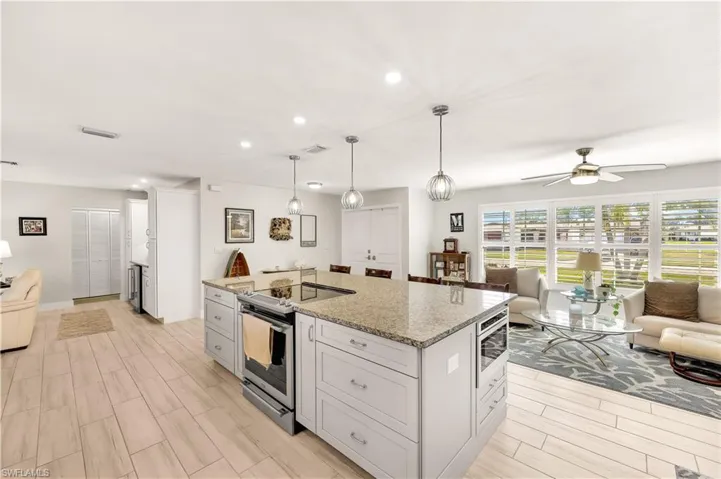 Kitchen with a kitchen island, white cabinets, hanging light fixtures, stainless steel appliances, and light stone countertops