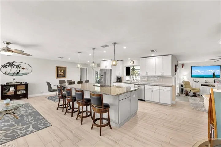 Kitchen with pendant lighting, stainless steel appliances, light stone countertops, white cabinets, and a kitchen island