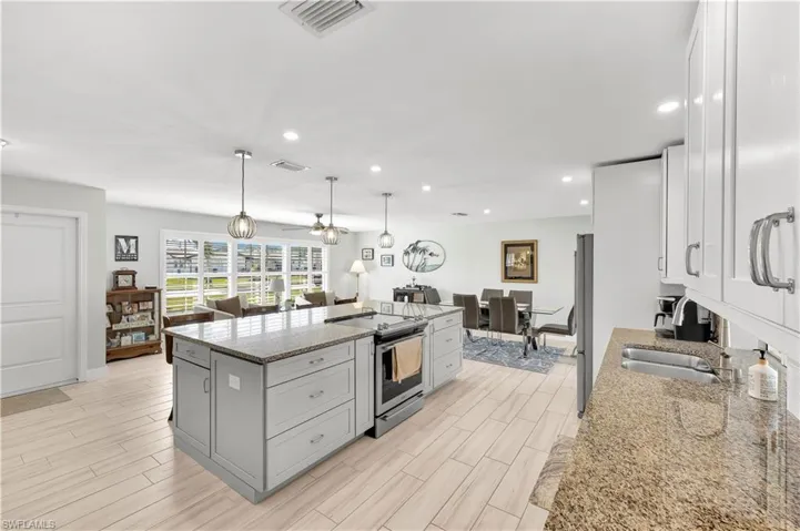 Kitchen with pendant lighting, a center island, ceiling fan, light stone counters, and stainless steel appliances