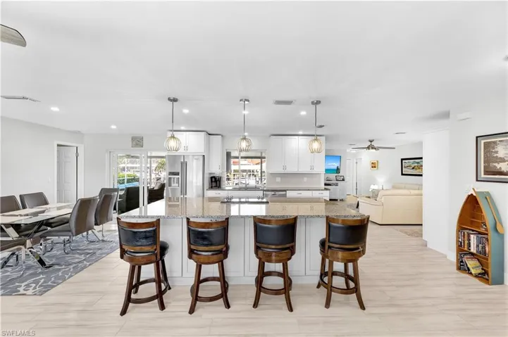Kitchen featuring high quality fridge, white cabinetry, a kitchen breakfast bar, hanging light fixtures, and light stone countertops