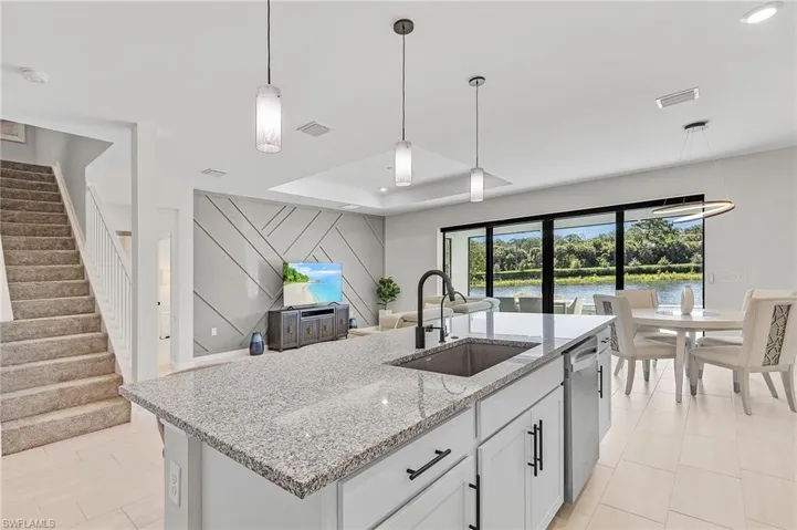 Open-concept living space featuring a central kitchen island with a granite-style countertop, white cabinetry with dark hardware, and a stainless steel sink with a dark faucet