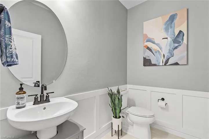 Powder room featuring a circular mirror, wall-mounted sink with dark bronze fixtures, wainscoting, and light gray wall paint