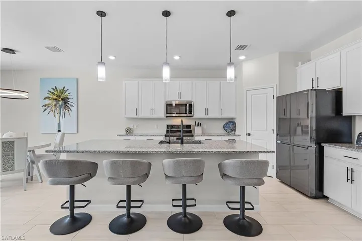 Gourmet kitchen featuring a large island with granite countertops, pendant lighting, white shaker cabinetry, and stainless-steel appliances