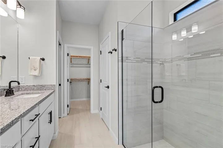 Modern bathroom featuring a glass-enclosed shower with tile surround, a single vanity with stone countertop, and light wood-finish flooring