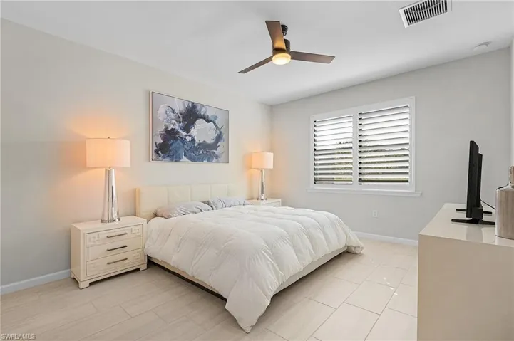 Light-toned rectangular tile flooring throughout, featuring a window with white plantation shutters, a ceiling fan with integrated lighting, and a neutral wall color