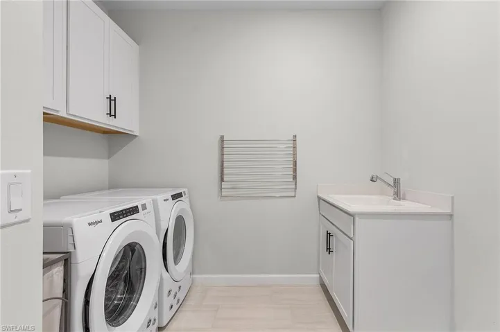 Laundry area featuring light wood-finish flooring, white cabinetry with dark hardware, a built-in sink with a chrome faucet, and a wall-mounted drying rack