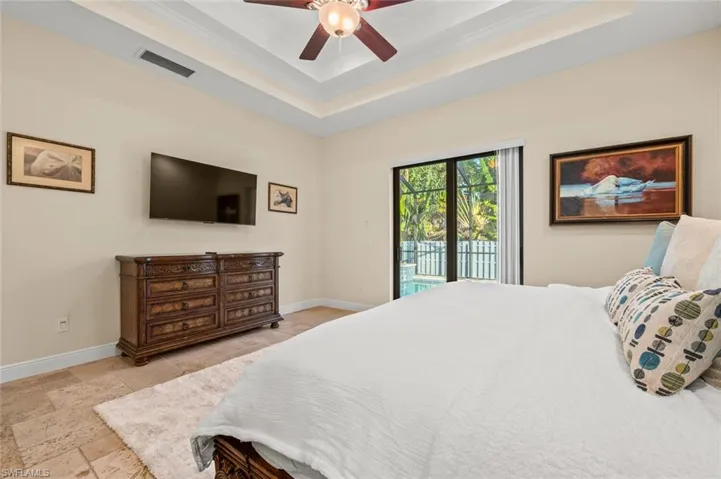 Bedroom with a tray ceiling, access to outside, crown molding, stone tile flooring, and a ceiling fan
