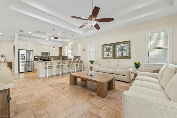 Living area with a raised ceiling, a ceiling fan, stone tile flooring, crown molding, and recessed lighting