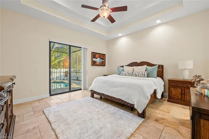 Bedroom with a raised ceiling, stone tile floors, ornamental molding, access to outside, and recessed lighting