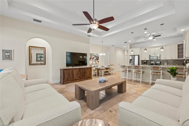 Living room featuring a raised ceiling, stone tile flooring, ceiling fan, crown molding, and recessed lighting