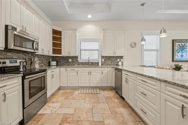 Kitchen with stainless steel appliances, a tray ceiling, decorative backsplash, recessed lighting, and white cabinets